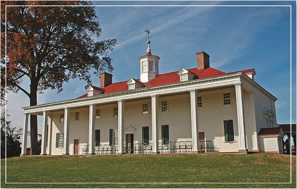 A historic building with a red roof surrounded by trees and lawn, under a blue sky.